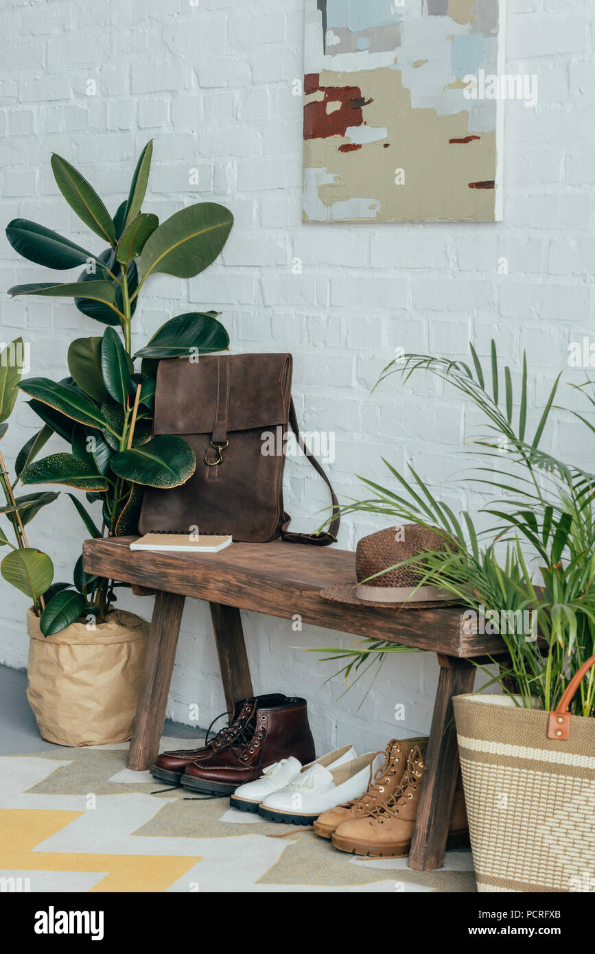 Verschiedene Schuhe unter Holzbank im Korridor zu Hause, Topfpflanzen auf dem Boden Stockfoto