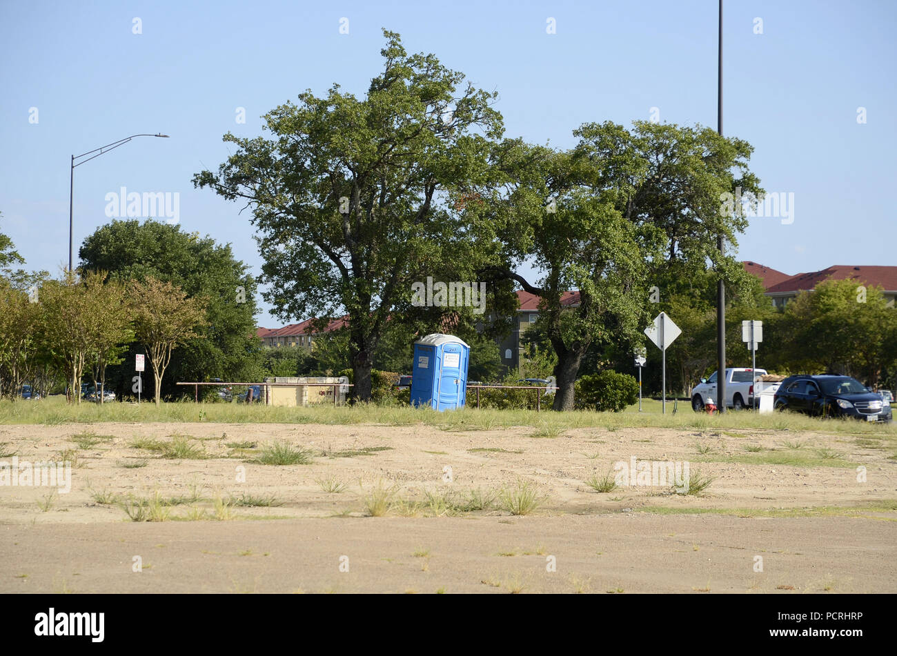 Single tragbare Toilette unter einigen Bäumen in einem leeren Grundstück durch eine Straße mit vorbeifahrenden Autos. Stockfoto