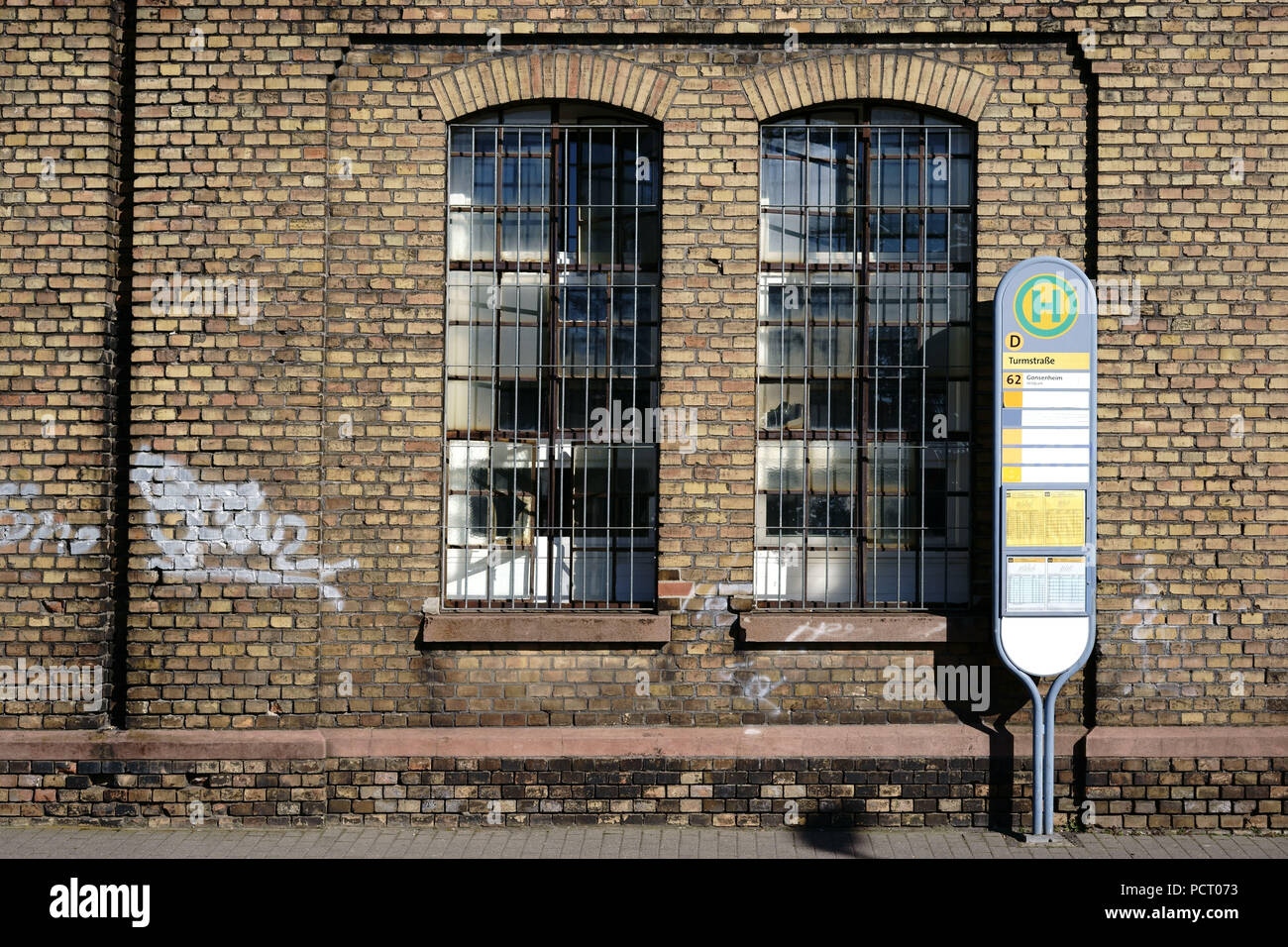 Ein haltestellenschild steht vor der Mauer einer stillgelegten Industriegebiet von einer alten Fabrik mit einem vergitterten Fenster Stockfoto