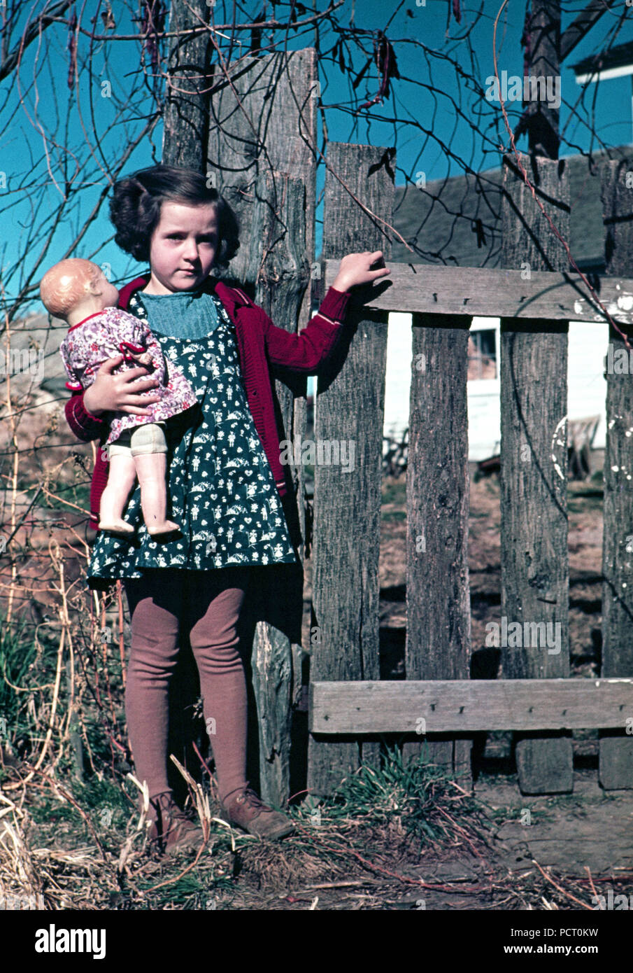 Mädchen mit Puppe steht durch Zaun ca 1941-1942 Stockfoto