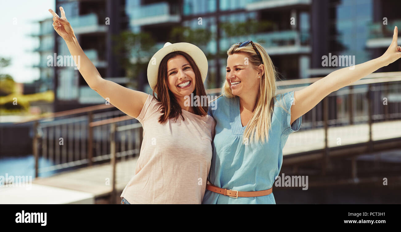 Zwei lachende Junge weibliche Freunde stehen Arm in Arm zusammen in der Stadt im Sommer eine gute Zeit Stockfoto