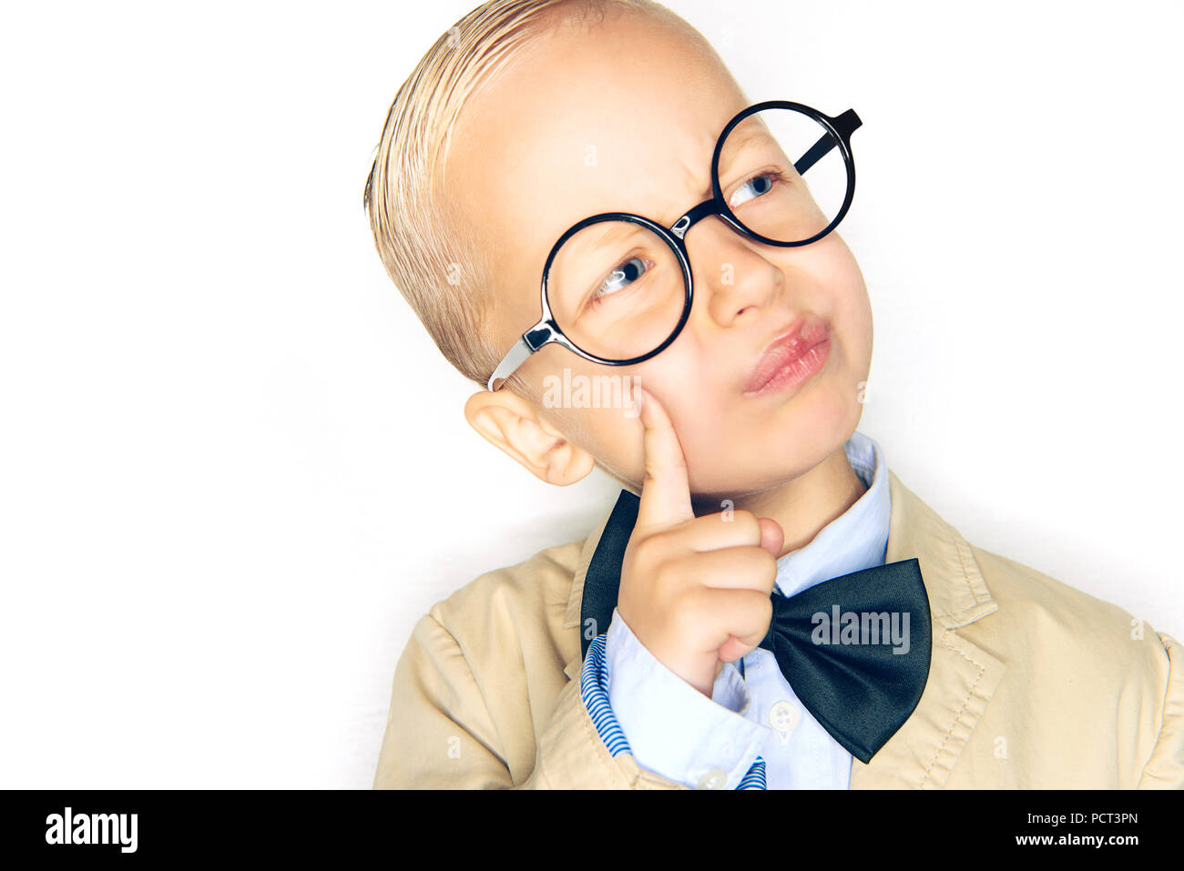 Adorable kleine blonde Junge im Anzug, bowtie und Gläser, tief in Gedanken, während vor einem weißen Hintergrund stehen Stockfoto