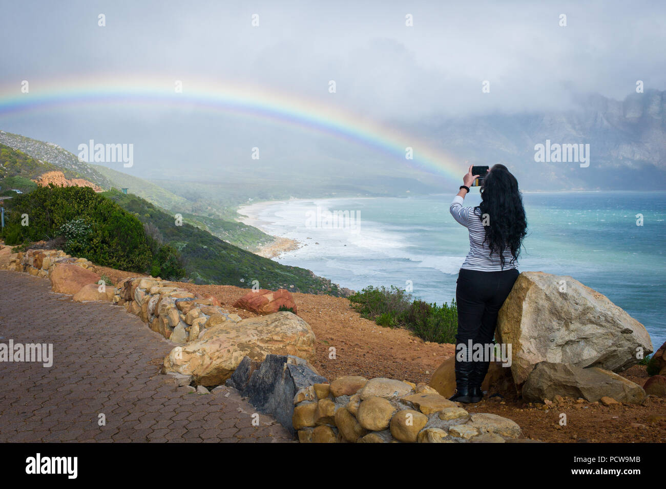 Frau unter Foto von malerischen Blick auf Regenbogen über Sandstrand in Kogel Bay, Western Cape Provinz, in Südafrika. Stockfoto