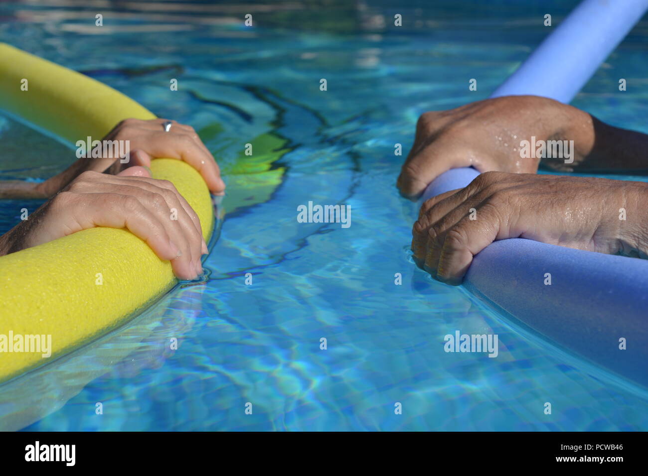 Paar im Pool, einander zugewandt, Floating mit pool Nudeln, selektiver Fokus auf Hände halten die Nudeln Stockfoto