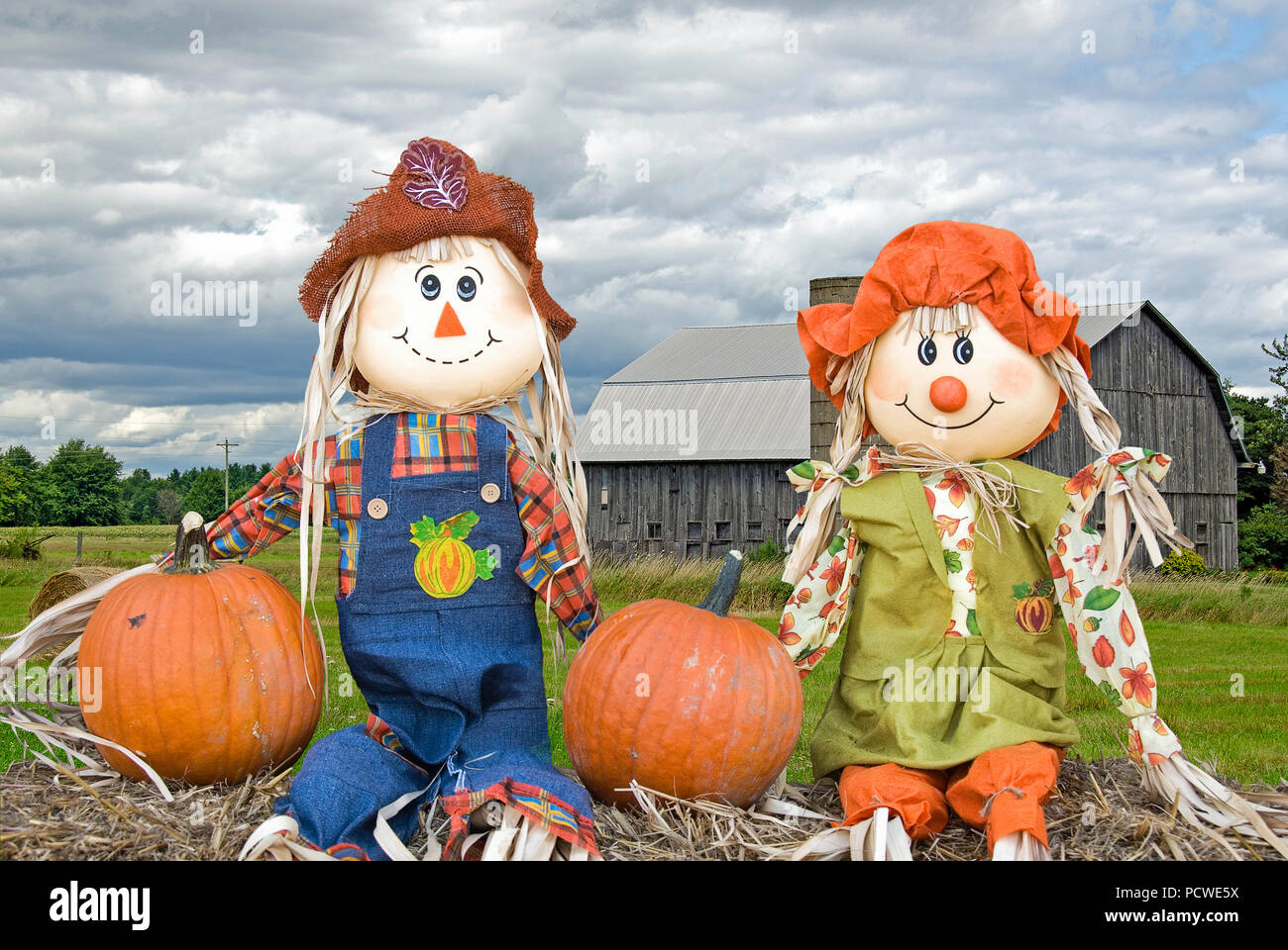 Beschreibung: Paar herbst Vogelscheuche Puppen auf Heu Ballen mit ländlichen Holz- Scheune im Hintergrund Stockfoto