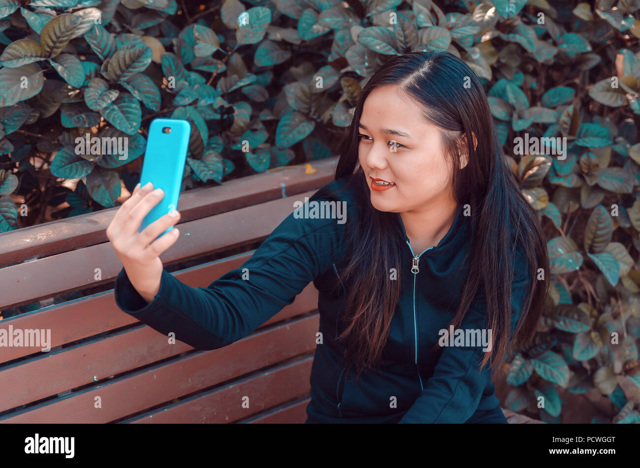 Lächelnde junge Dame unter selfie auf einer Bank mit Ihrem Smart Phone Stockfoto