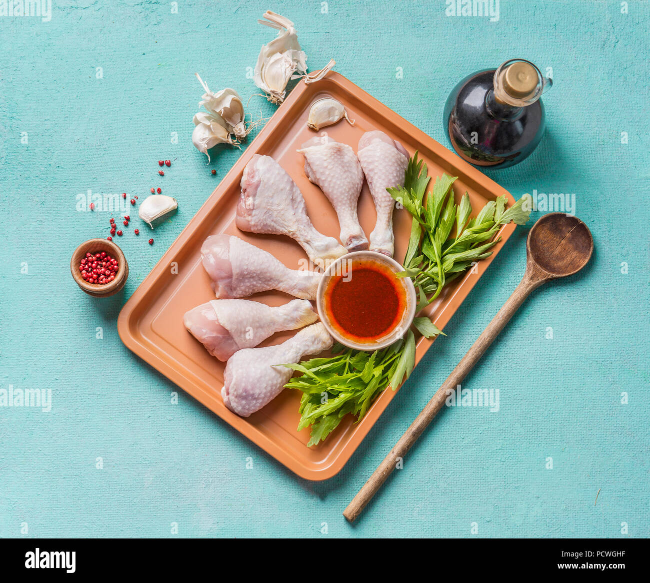 Kochen Vorbereitung von Rohstoffen Chicken Drumsticks. Raw Hähnchenschenkel  auf Platte mit Kräutern, Gewürzen, Soße und Kochlöffel auf hellblauem  Hintergrund, oben vi Stockfotografie - Alamy