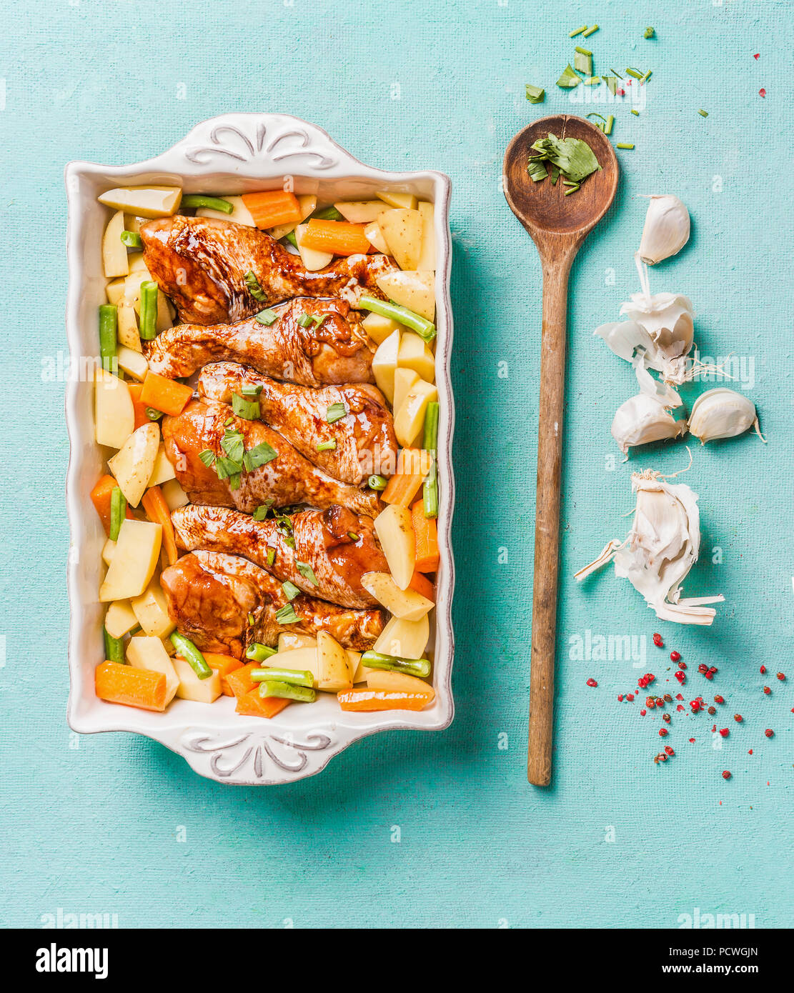 Blick von oben auf die Chicken Drumsticks mit Gemüse in backen Auflauf auf hellblauem Hintergrund mit Kochlöffel und Kräuter und Gewürze. Gesunde Ernährung Stockfoto