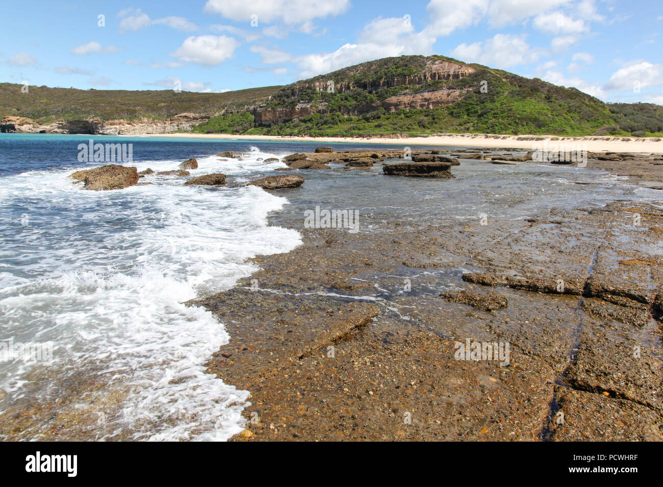 Welle rollt über die Felsen am flachen Felsen südlich von Moonee - Catherine Hill Bay an der New South Wales Central Coast. Stockfoto