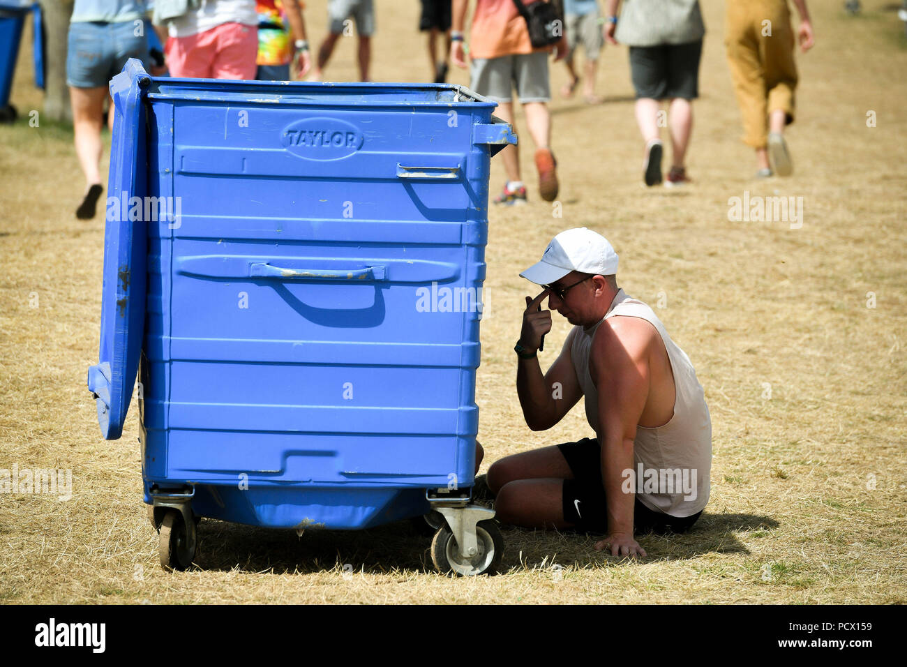 Ein Mann findet Schatten neben einem Mülleimer in der heißen, sonnigen Wetter während Bestival am Lulworth Immobilien in Dorset. Stockfoto
