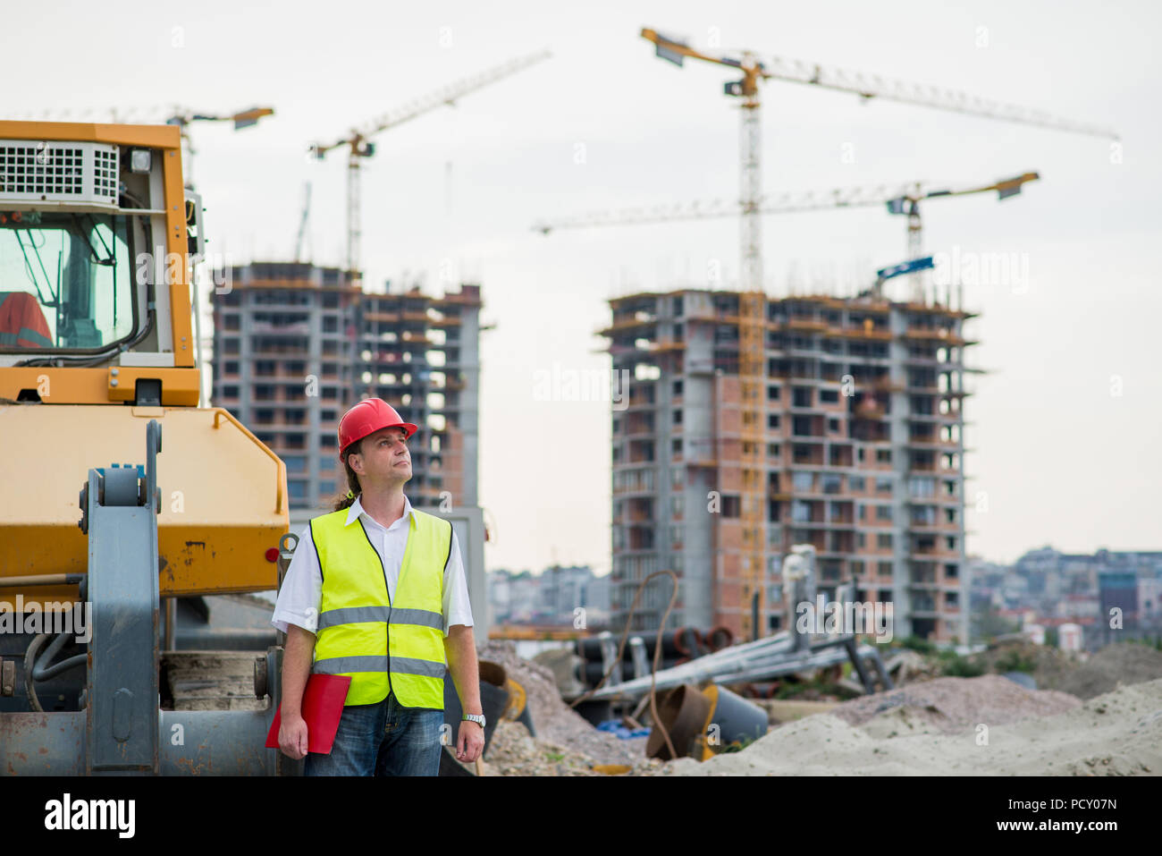 Ingenieur vor der Bagger auf einer Baustelle mit Gebäuden und Krane im Hintergrund Stockfoto