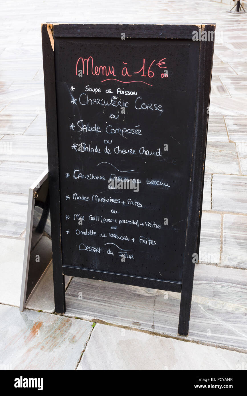 Eine Restaurantmenü-Tafel mit französischen Gerichten, die mit Kreide auf einem Straßenpflaster in Bastia, Korsika, Frankreich geschrieben sind. Stockfoto