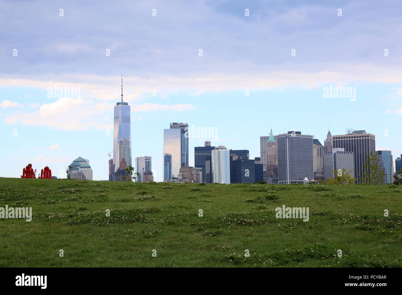 Paar sitzen auf zwei rote Gartenstühle auf Governors Island Hügel beobachten Bankenviertel Skyline, Governors Island am 4. Juli 2017 in New York, Stockfoto