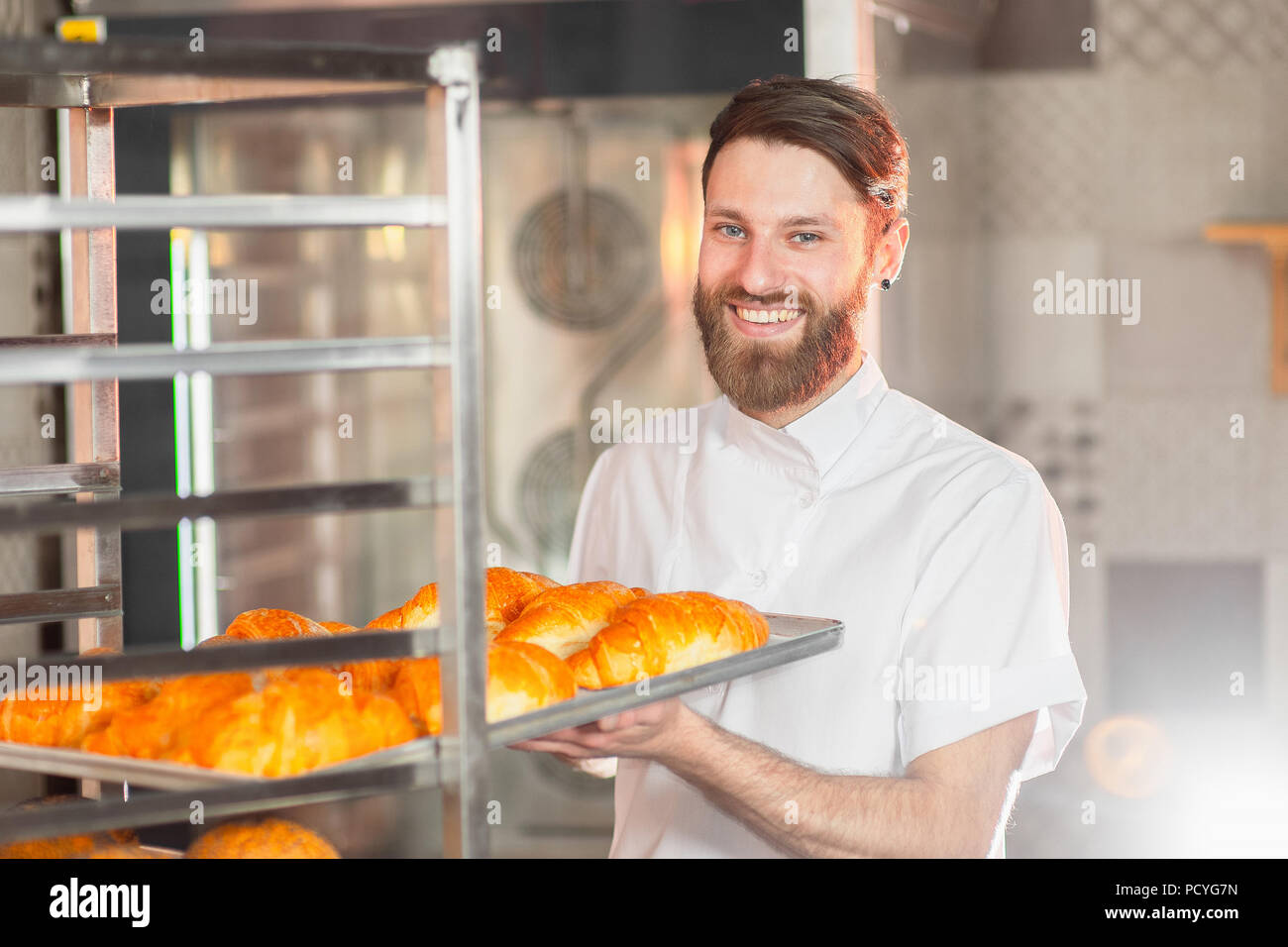 Ein junger hübscher Baker nimmt heiße frisch aus dem Ofen backen in der Bäckerei. Stockfoto