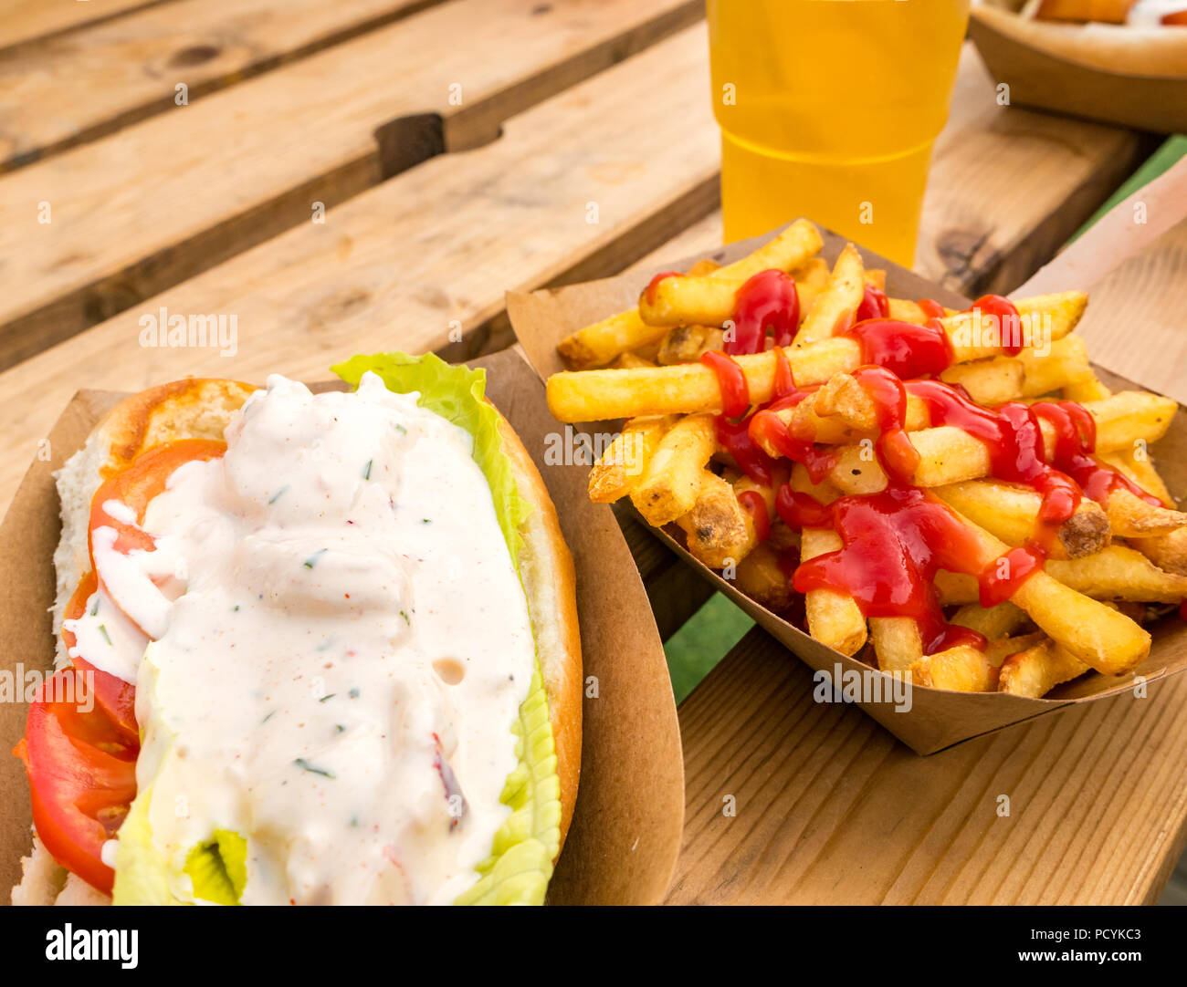 Essen zum Mitnehmen: Hummerrolle mit Pommes Frites oder pommes Frites Mit Ketchup und einem halben Pint Lagerbier in einem Plastikglas auf einem Picknicktisch im Freien Stockfoto