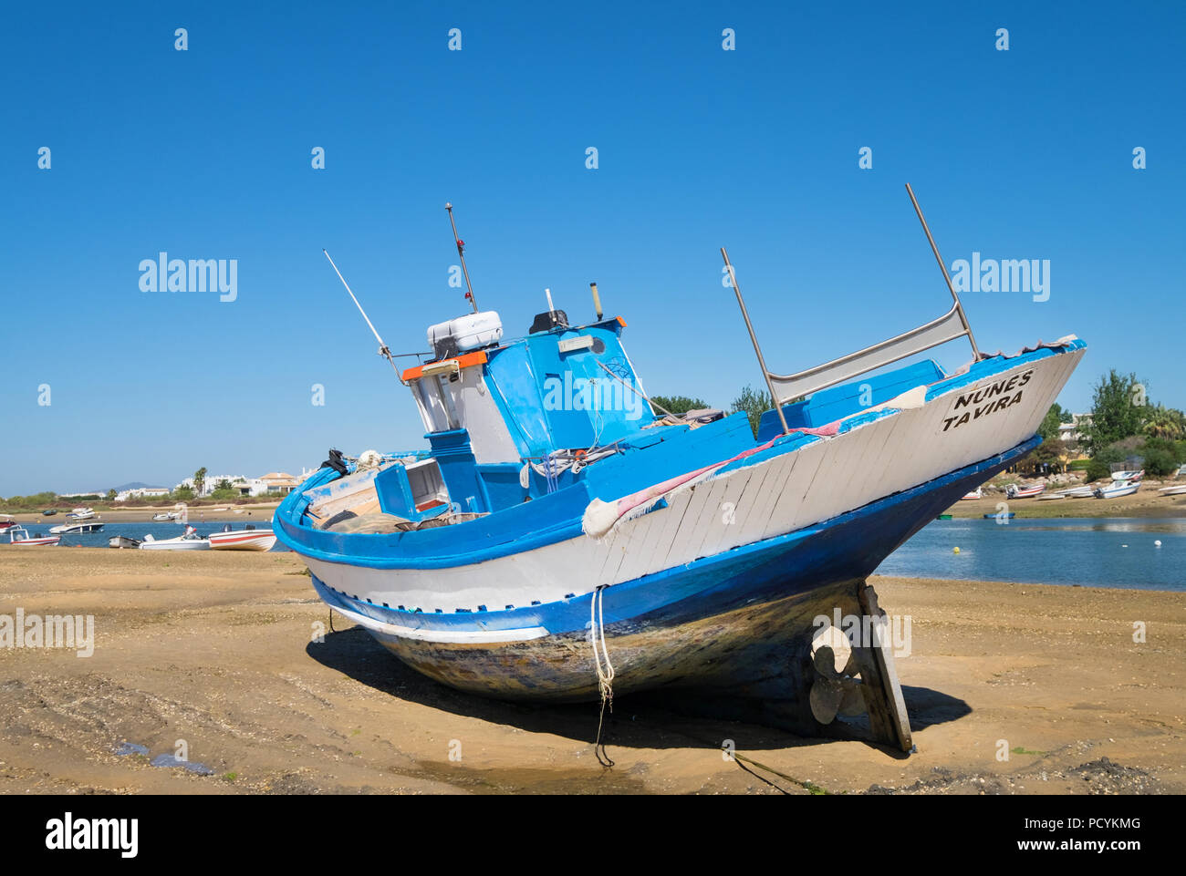 Ein Fischerboot bei Ebbe am Strand mit Cabanas Cabanas Dorf im Hintergrund, im Cabanas in der Algarve, Portugal Stockfoto