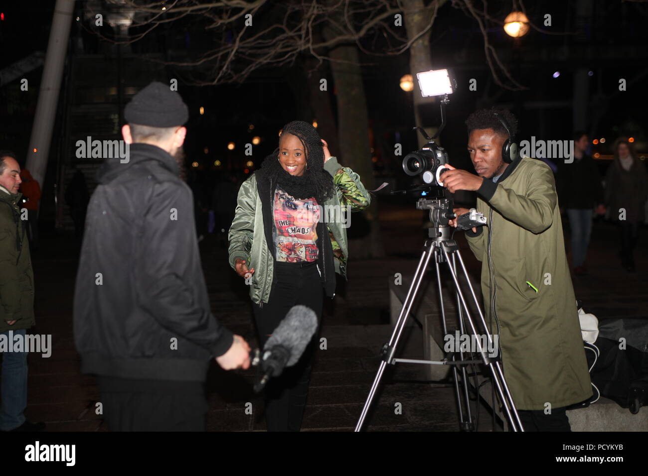 Die mobile TV-Crew dreht am Winterabend am Ufer der Themse in London ein Videointerview auf DSLR mit einem afrikanischen Kameramann, der die Szene filmt. Stockfoto