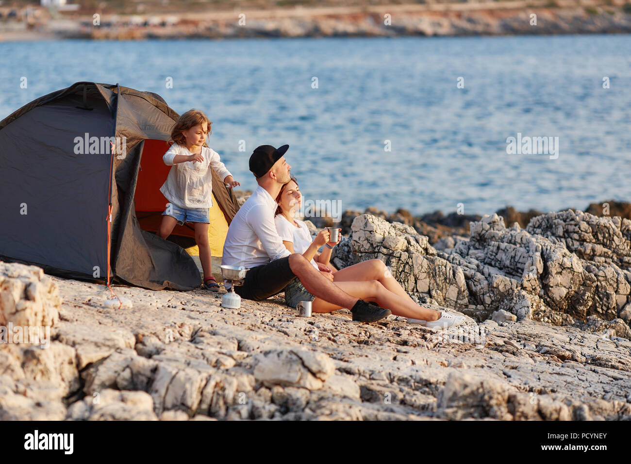 Freundliche ehrliche Familie ruht auf felsigen Strand in der Nähe von Zelt. Stockfoto