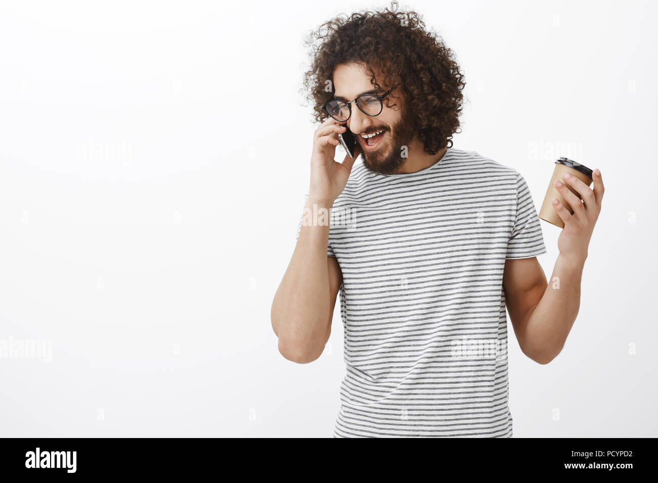 Studio shot zufrieden glücklich nach Freund mit lockigem Haar, Brille und stilvolle Gestreiftes T-Shirt, Tasse und gestikulierend während des Sprechens auf Stockfoto