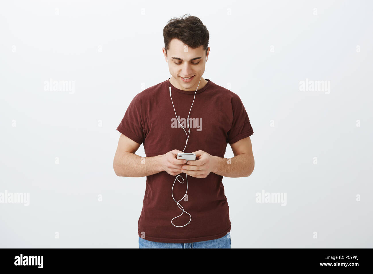 Innen- schuss von Happy europäischen Freund im casual t-shirt, Smartphone und Kommissionierung Song im Kopfhörer zu hören, Messaging mit Freundin oder Pi Stockfoto