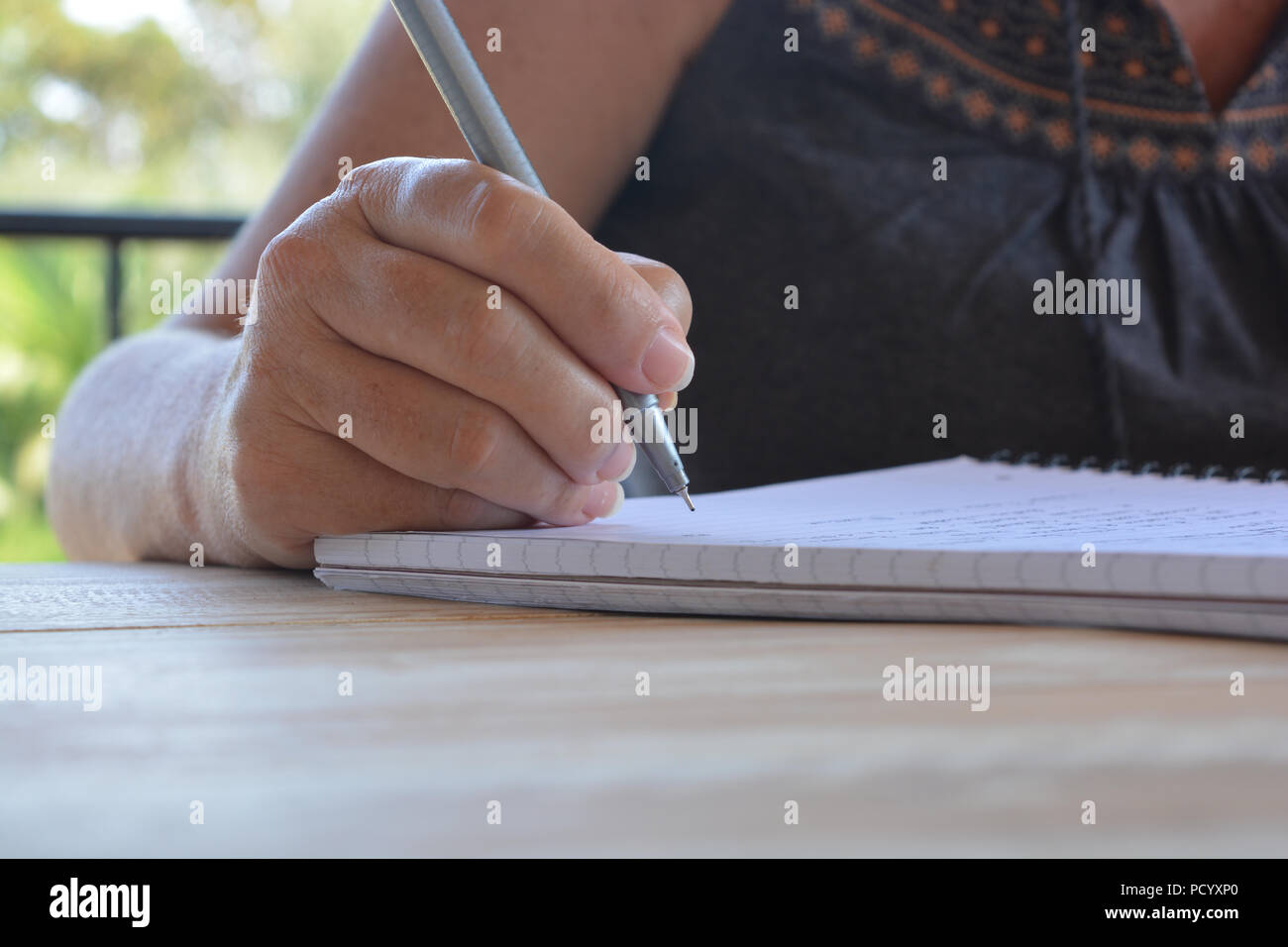 Frau an einem Tisch sitzen, schreiben in einer Spirale gebundenes Notizbuch, selektiver Fokus auf pen Feder in der Hand Stockfoto