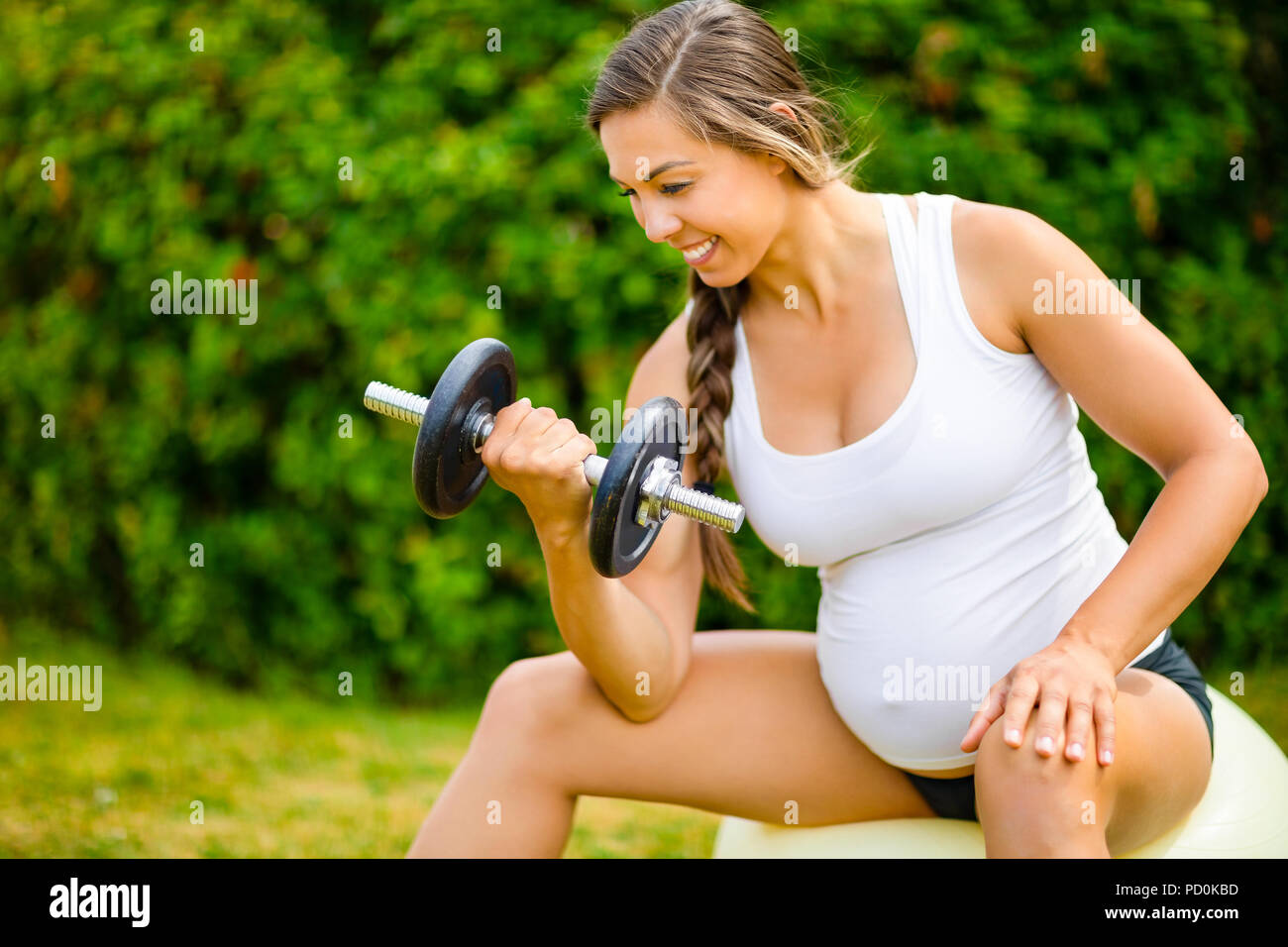 Schwangere Frau Hanteln beim Sitzen auf Übung Kugel Stockfoto