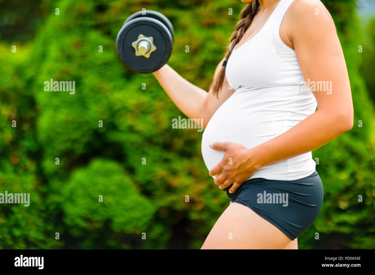 Schwangere Frau berühren Magen während des Trainings mit Hantel Stockfoto
