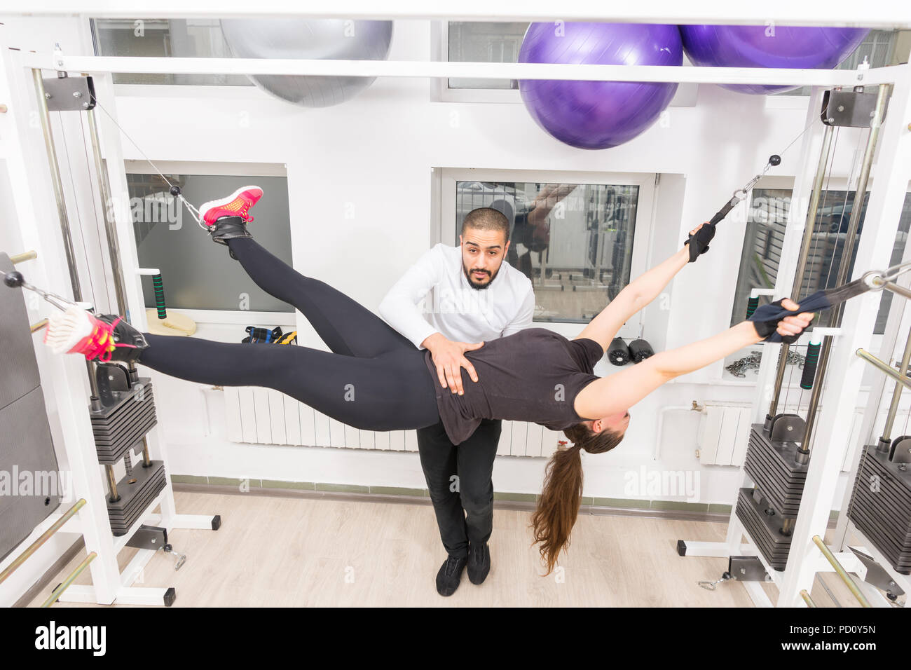 Trainer helfen Frau mit Abdominal- Übung wie Sie hält Schwarze Lederriemen, die Sie in der Luft aussetzen Stockfoto
