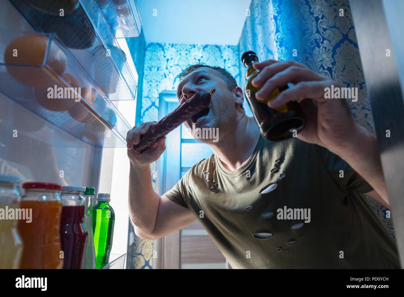 Gierig Mann einen großen Bissen von einer Salami Wurst, wie er in der  offenen Tür von seinem Kühlschrank mit einem kalten Bier in der anderen  Hand steht Stockfotografie - Alamy
