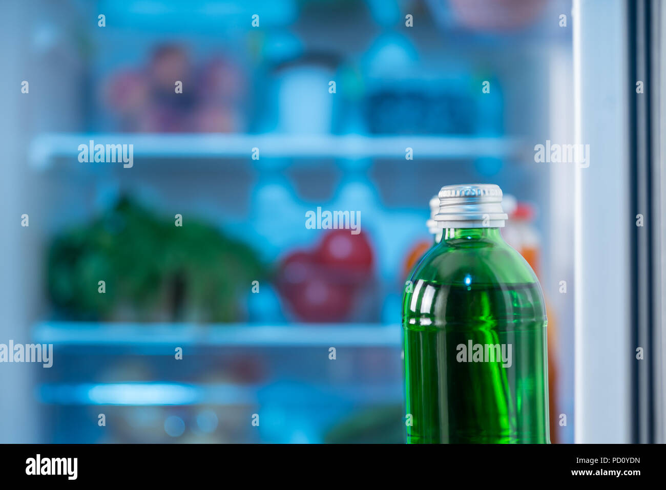 Grüne Flasche mit Saft oder Soda in einem offenen Kühlschrank Tür mit selektiven Fokus und ein verschwommener Blick in die Regale mit Kopie Raum Stockfoto