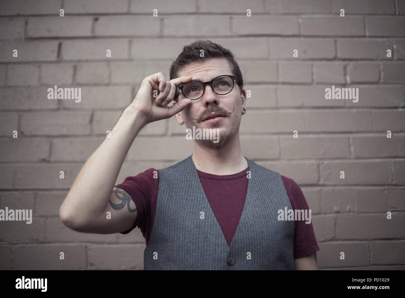 Weißen jungen Mann mit einem Tattoo im Arm, curly Schnurrbart, und Spitzbart seinen braunen vintage Brille zuvorkommend. Stockfoto
