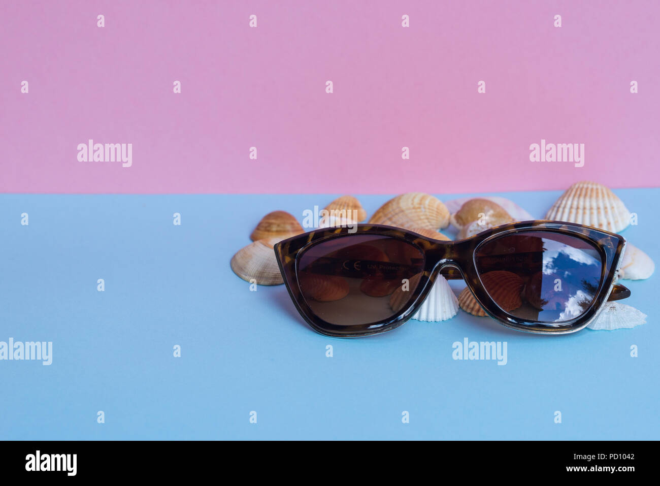 Verschiedene Arten von Muscheln und eine Sonnenbrille auf Hellblau und Rosa Hintergrund. Minimalistisches Bild, das Erfassen der Geist der Sommer. Acanthocardia Rohr Stockfoto