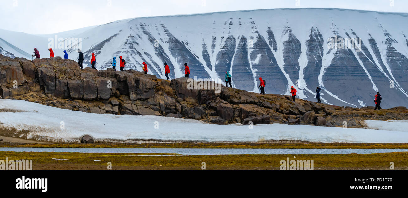 Eine Linie der Wanderer Queren einer Ridge vor schneebedeckten Bergen in Svalbard. Stockfoto