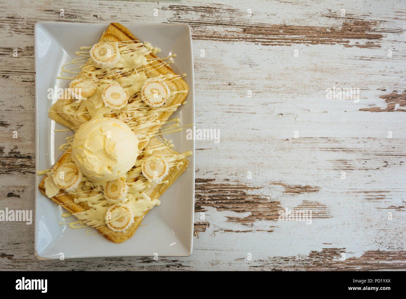 Belgische Waffeln mit geschmolzener weißer Schokolade, Vanilleeis und Kokosraspeln auf hellen Hintergrund. Stockfoto