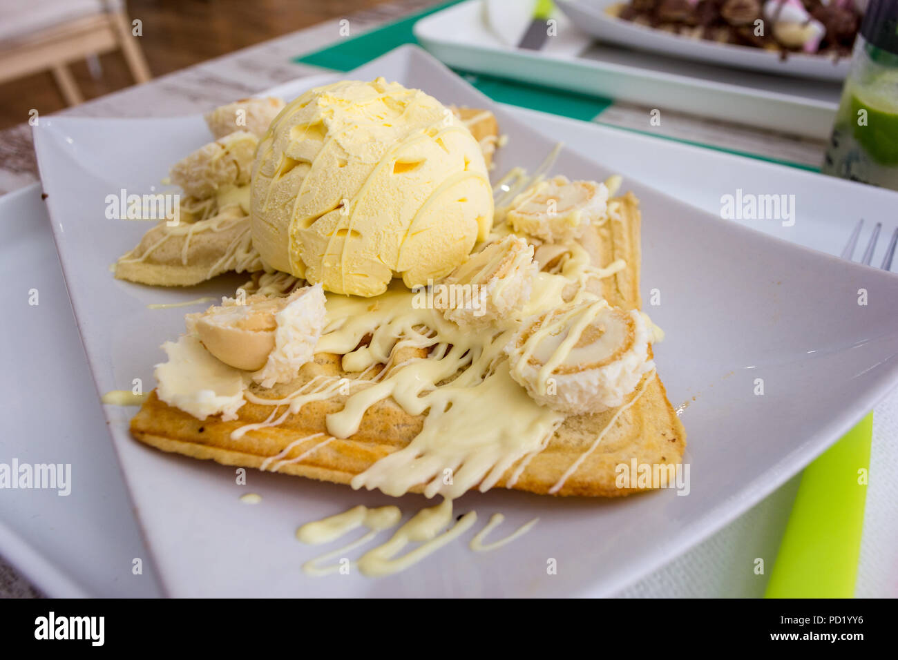 Belgische Waffeln mit geschmolzener weißer Schokolade, Vanilleeis und Kokosraspeln auf hellen Hintergrund. Stockfoto