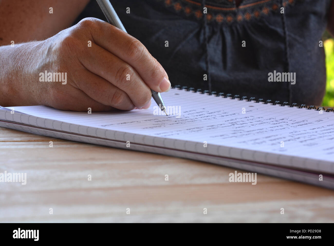 Frau an einem Tisch sitzen, schreiben in einer Spirale gebundenes Notizbuch, selektiver Fokus auf pen Feder in der Hand Stockfoto