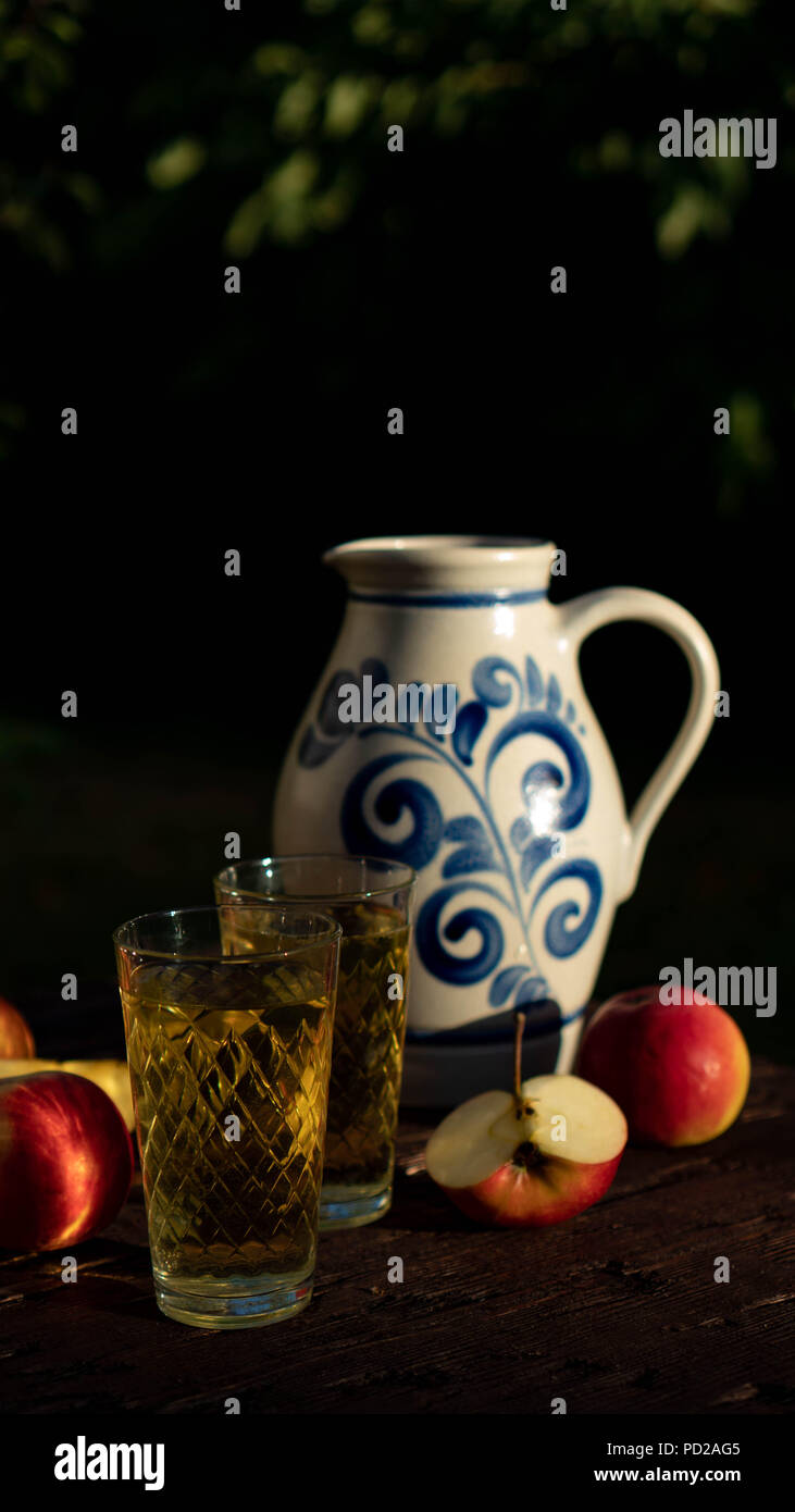 Traditionelle apple Wein in der Stadt Frankfurt am Main in Hessen. Einen Krug Wein ist auf einer alten hölzernen Tisch in den Garten, um ihn herum sind Äpfel Stockfoto