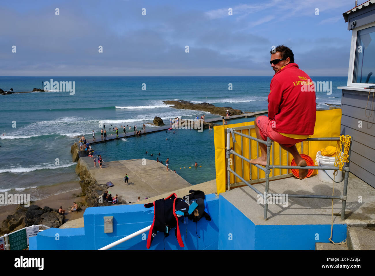 Bude, Cornwall, UK. RNLI Rettungsschwimmer wacht über Schwimmer genießen das warme Wetter und das Wasser in einer Bude der semi-natürlichen Badebecken Stockfoto