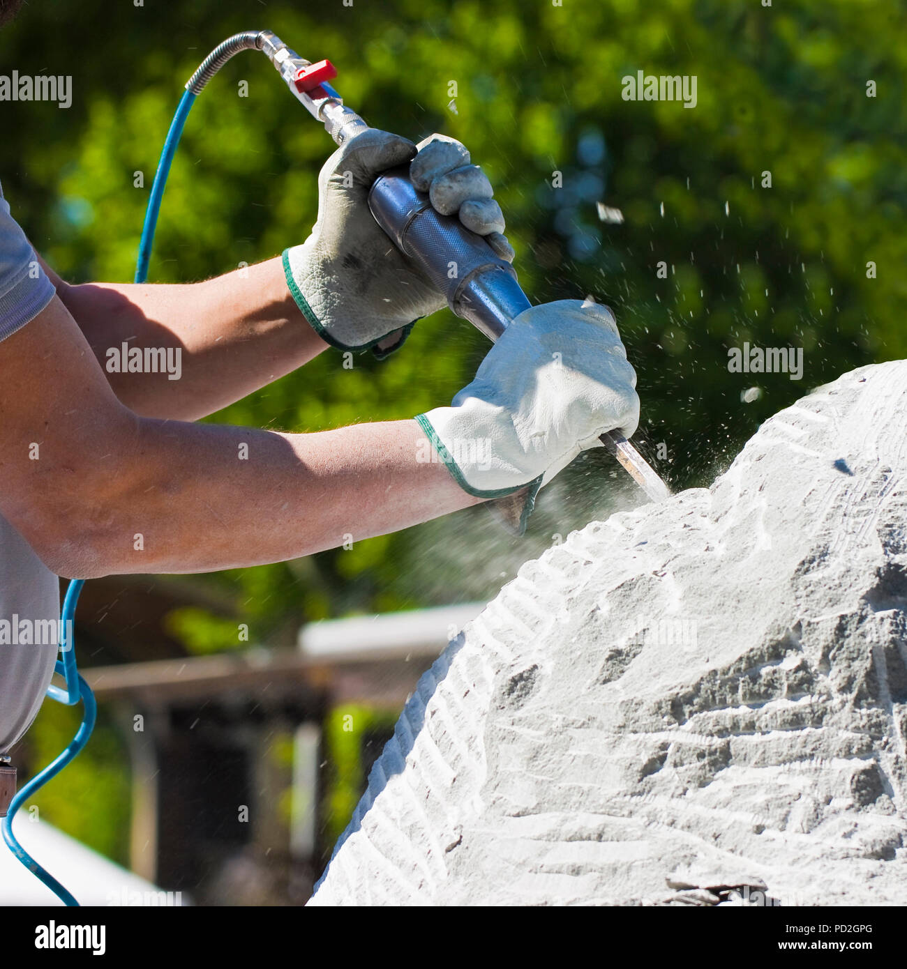 Junger Mann bei der Arbeit mit Druckluft Meißel und Schutzhandschuhe zu schnitzen einen Steinblock Stockfoto