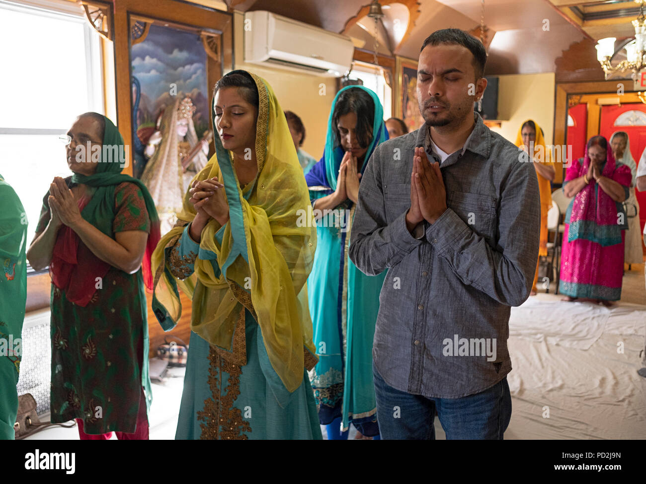 Ein Mann und eine Gruppe von Frauen mit gefalteten Händen in Gebet und Meditation zu einem Hindu Tempel in South Ozone Park, Queens, New York. Stockfoto