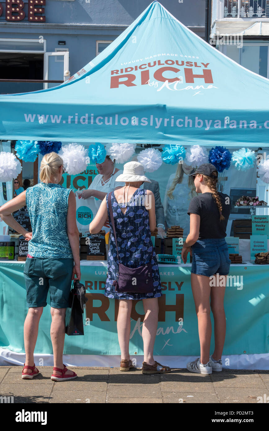 Drei Damen an einem süsswaren Stall oder Messestand während der Cowes Week auf der Insel Wight. Kauf von Fudge und Süßigkeiten aus einem Markt im Sommer Stall. Stockfoto