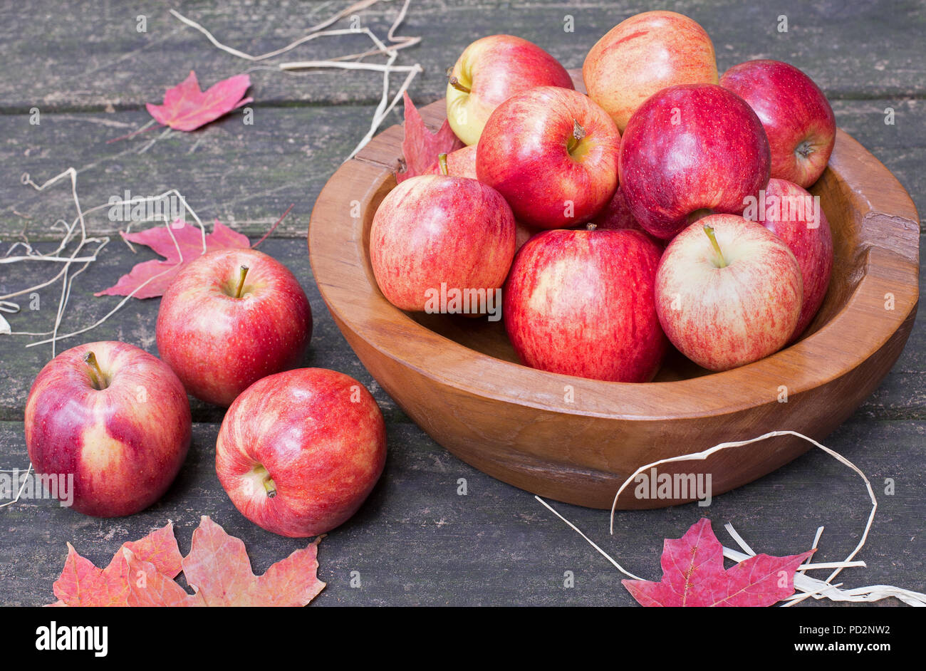 Rote Äpfel und Schüssel mit Herbstlaub auf einem rustikalen hölzernen Oberfläche Stockfoto