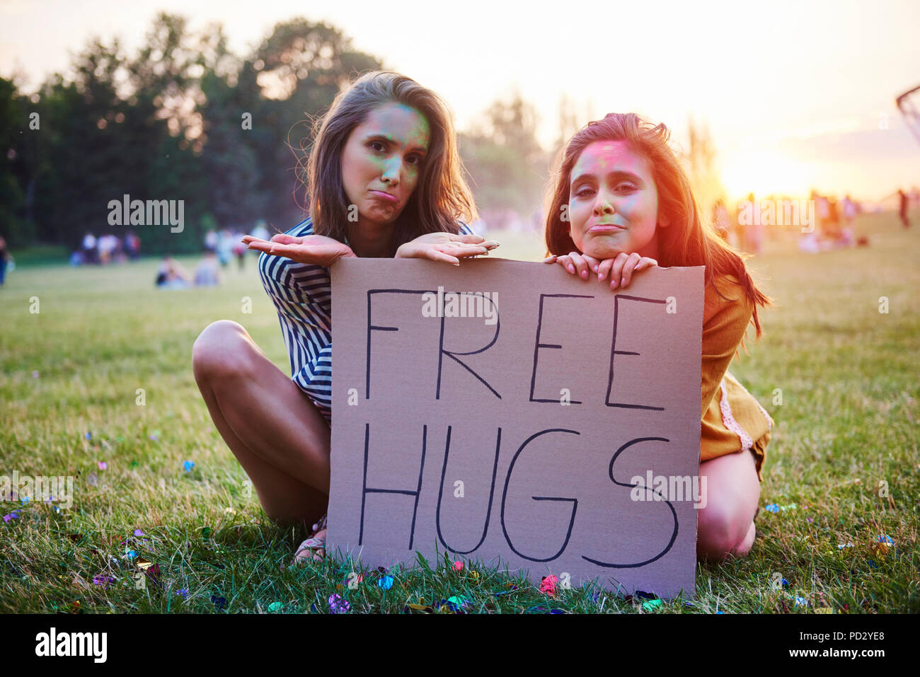 Junge Frauen sitzen auf Gras holding Free hugs Zeichen im Holi Festival, Porträt Stockfoto