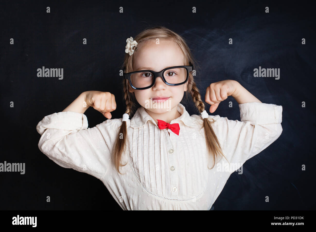 Fröhliches kleines Mädchen in Klasse Zimmer mit Schiefertafel Hintergrund. Zurück zu Schule, School Girl Power, Kreativität und Bildung Konzept Stockfoto