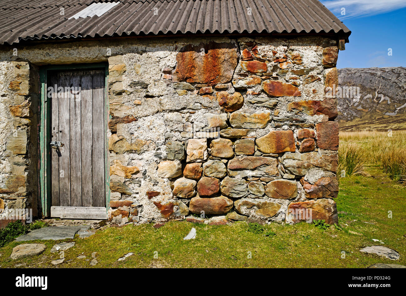 Alten verwitterten hölzernen Tür und Mauer von traditionellen Steinhaus mit Wellblechdach in abgelegenen moorland Lage in Sutherland, Schottland, Großbritannien. Stockfoto