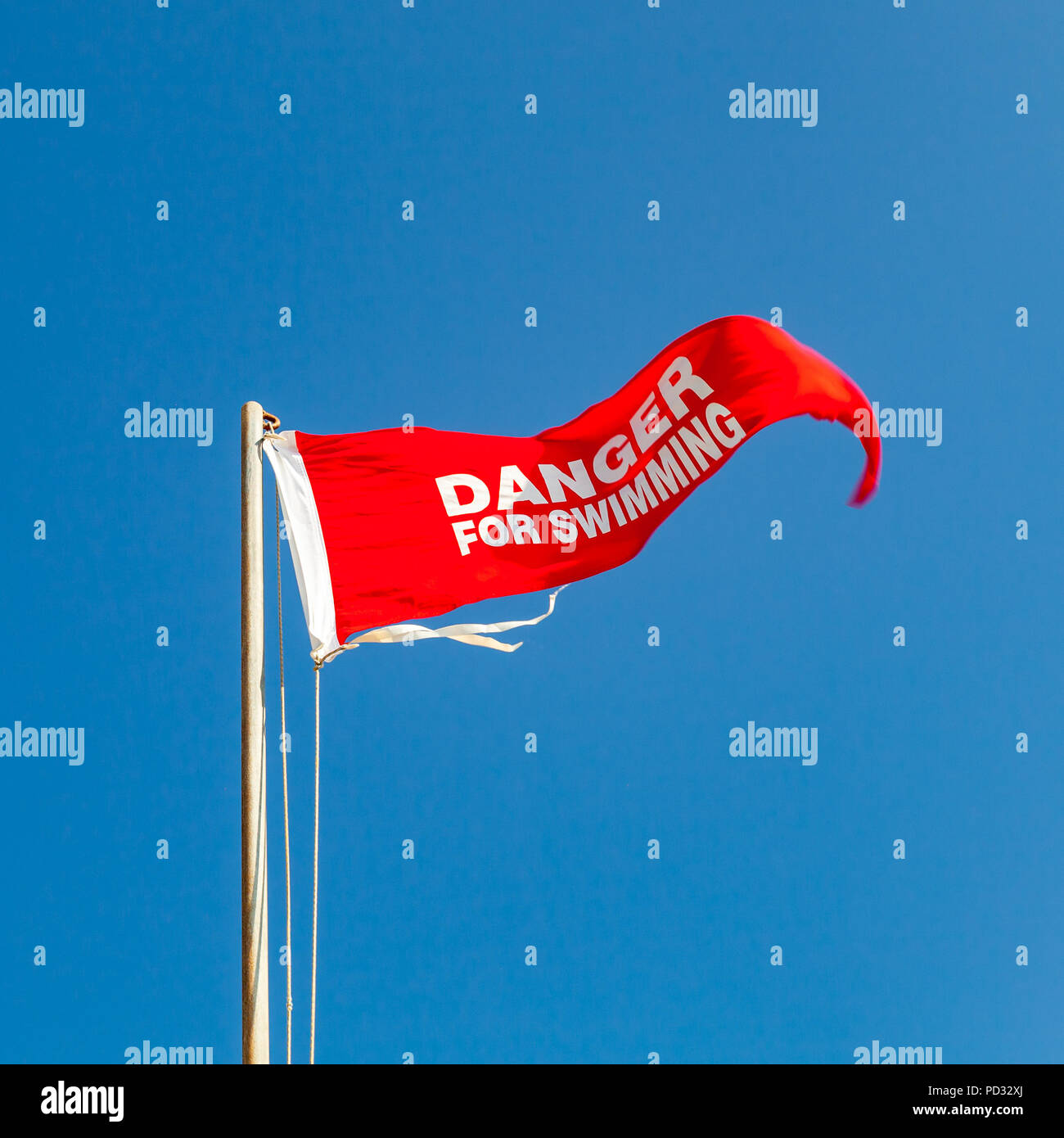 Gefahr für das Schwimmen. Rote Warnlampe Flagge am Strand wellenartig über blauen Himmel. Close-up Platz Foto Stockfoto