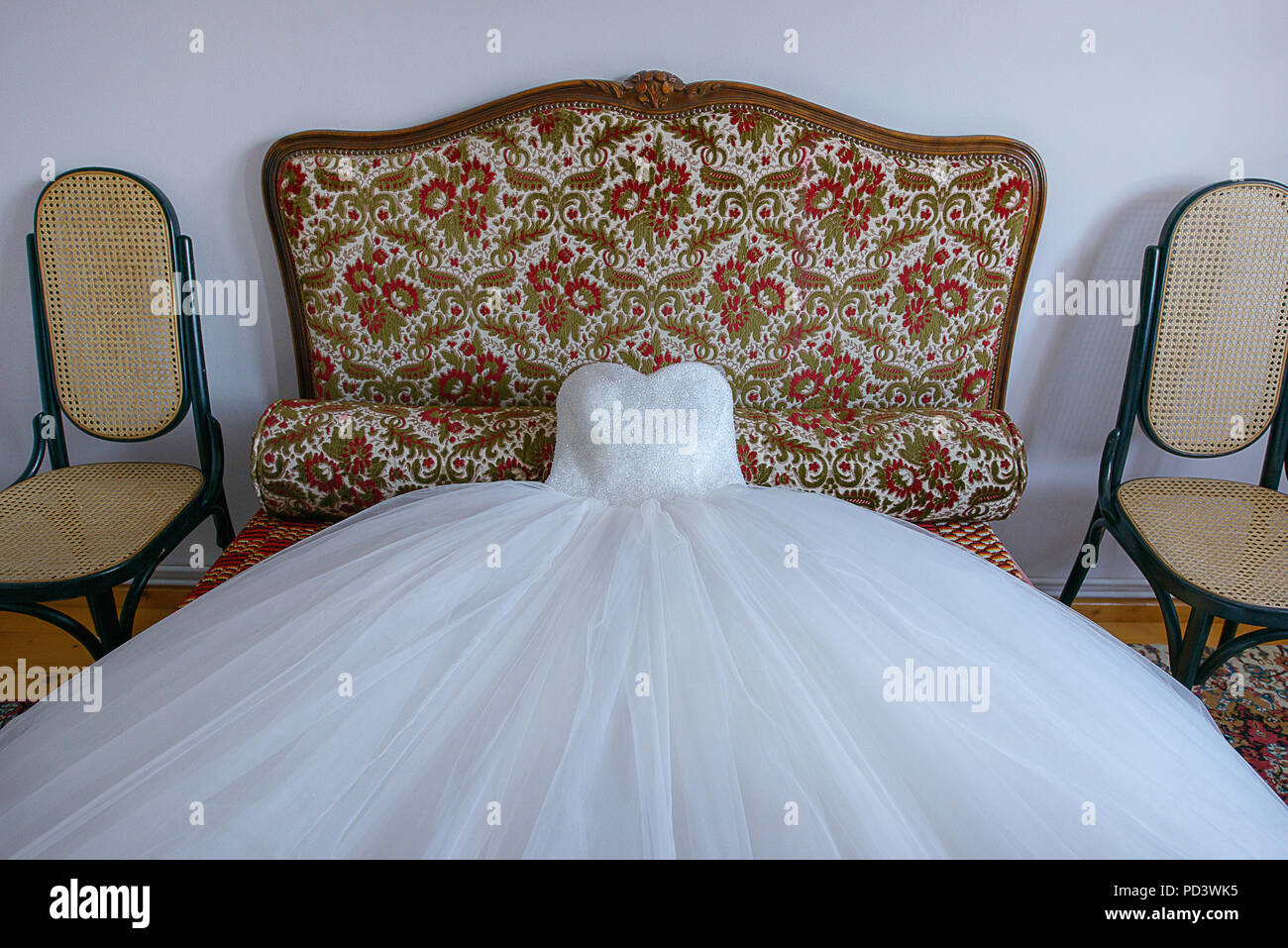 Atemberaubendes Ballkleid Hochzeitskleid verteilen sich auf ein kleines Sofa, bereit für die Braut in der Vorbereitung für den grossen Tag Stockfoto