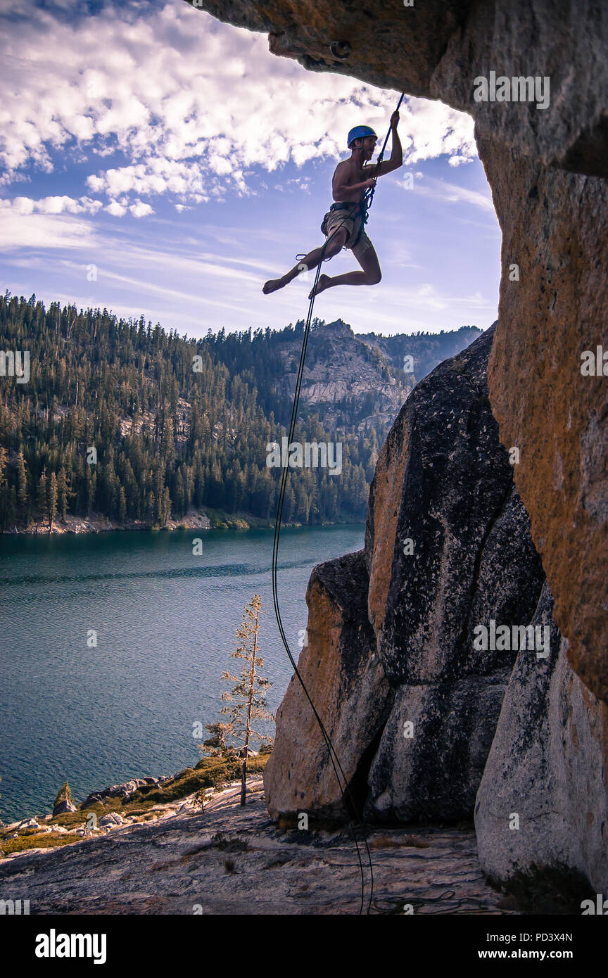 Junge männliche Kletterer baumelnd auf Seil aus Fels, High Sierras, Kalifornien, USA Stockfoto