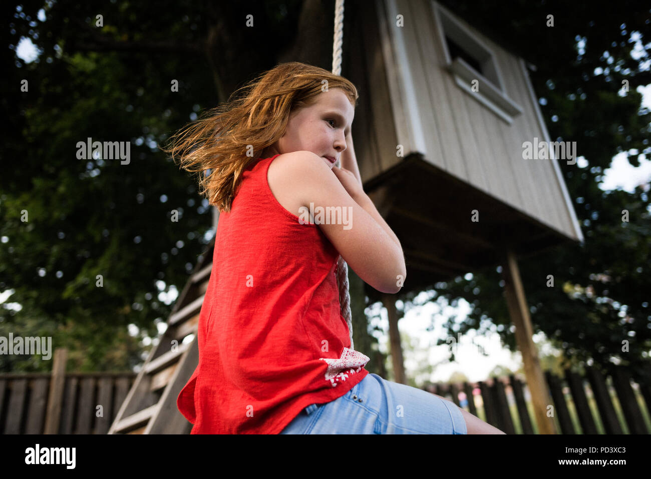 Mädchen Schwingen am Seil unter Tree House Stockfoto