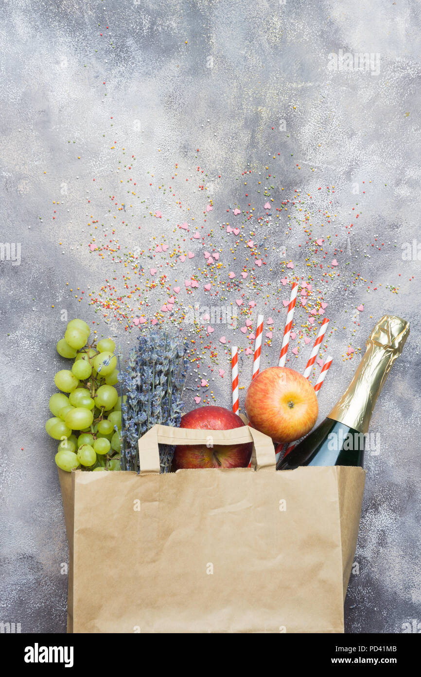 Wein, Obst, Blumen (für die Party oder ein Picknick in einem Paper Craft pack auf grauem Beton Hintergrund). Ansicht von oben. Stockfoto